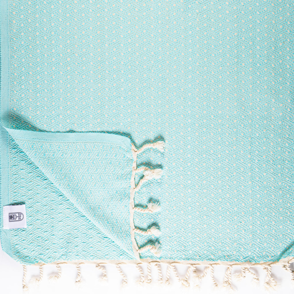 Teal towel with white tassels on a matching background