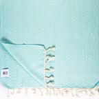 Teal towel with white tassels on a matching background